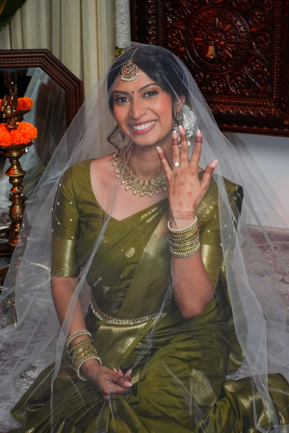 A smiling bride in a green sari and veil, showing her hand